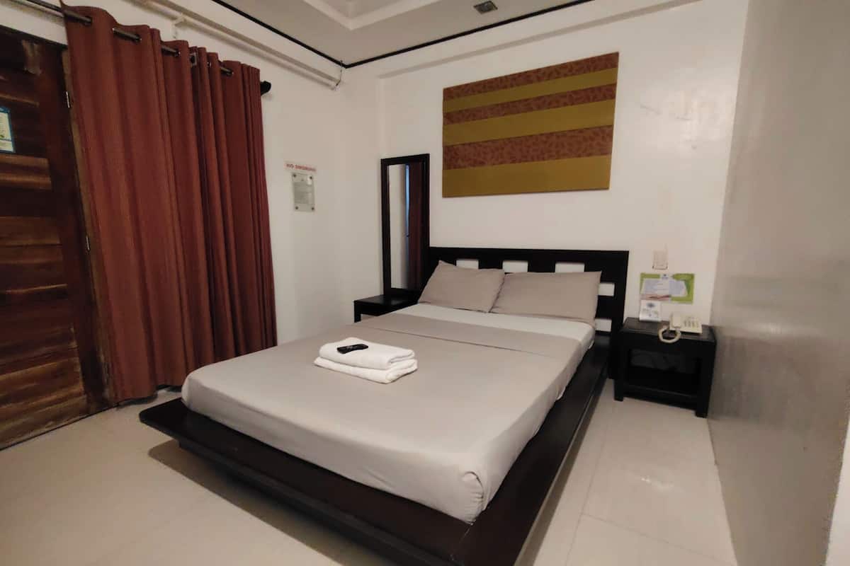 A hotel room with a bed, a nightstand, a wall-mounted telephone, and a 'No Smoking' sign.