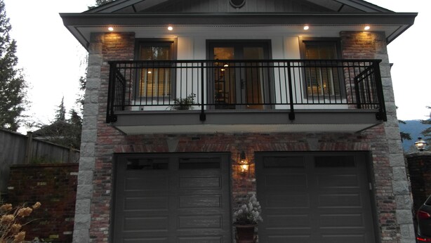 Een twee verdiepingen tellend huis met een balkon, twee garagepoorten en een stenen gevel.