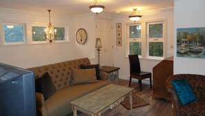 Een woonkamer met een bank, salontafel en stoelen. Op de muur hangt een klok en een schilderij.