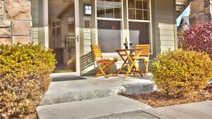 A house with a stone facade, a porch with wooden chairs and a table, and a small garden with shrubs. - Luxury condo, Walk to Theater & Restaurants, K & Q beds,  private gar. & grill (Park City)