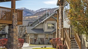 A residential building with a stone facade, a wooden balcony, and a view of mountains in the background. - Luxury condo, Walk to Theater & Restaurants, K & Q beds,  private gar. & grill (Park City)