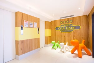 Een hotel receptie met een houten wand, een receptiebalie en een bordje voor Click Hotel. Op de vloer liggen drie kleine, kleurrijke decoraties in de vorm van dieren.
