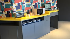 A kitchen with a microwave, toaster, and coffee maker on a yellow countertop, with a colorful abstract wall behind. - Click Hotel - Taipei Main Station Branch (Taipei)