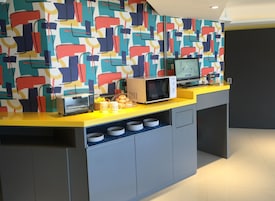 Een keuken met een magnetron, broodrooster en koffiezetapparaat op een geel aanrecht, met een kleurrijke abstracte muur erachter.