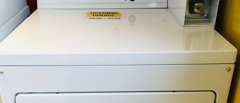 A Whirlpool commercial dryer with a control panel, a yellow sticker indicating operating hours, and a metal rack on top.
