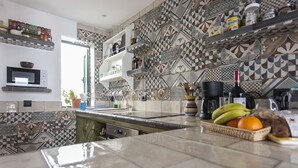 Una cucina con piastrelle decorate, un forno a microonde, una macchina per il caffè e un cesto di frutta.