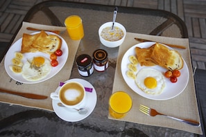 Una bandeja de desayuno con tostadas, huevos, tomates y un vaso de jugo de naranja.