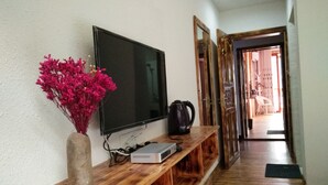 A wooden console table with a flat-screen TV, a small electronic device, and a vase of pink flowers. - National Park MINI Inn - Yangjiajie (Zhangjiajie)