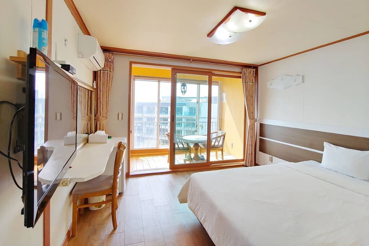 A hotel room with a bed, a desk, a chair, a television, and a sliding glass door to the balcony.