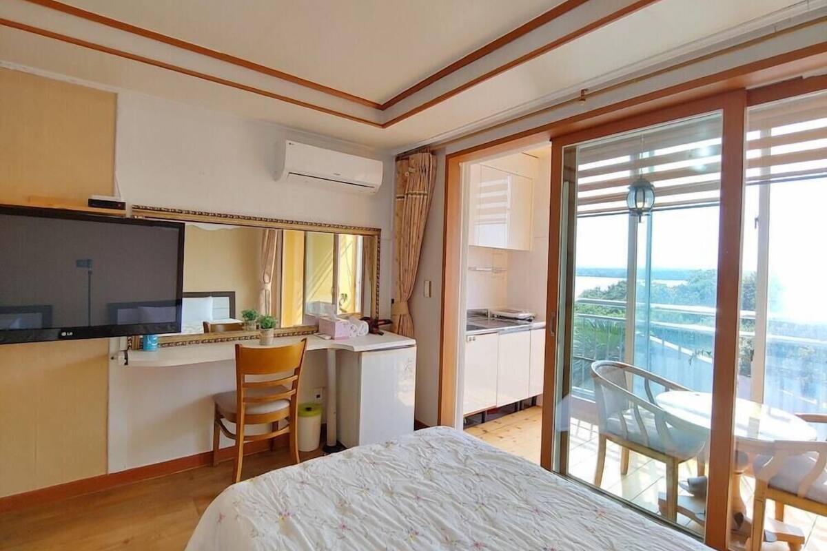A hotel room with a bed, a desk, a TV, a balcony with a view, and a sliding door.