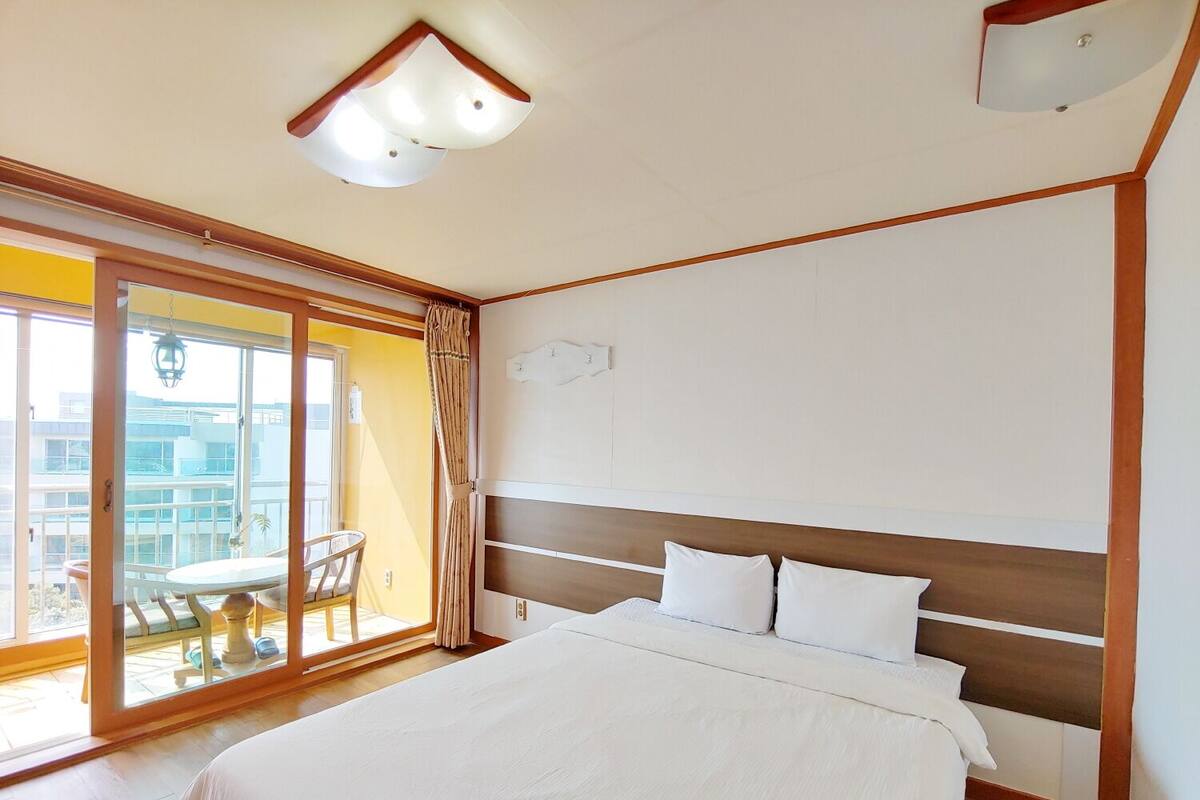 A hotel room with a large bed, a view through a sliding glass door to an outdoor area, and a ceiling light fixture.