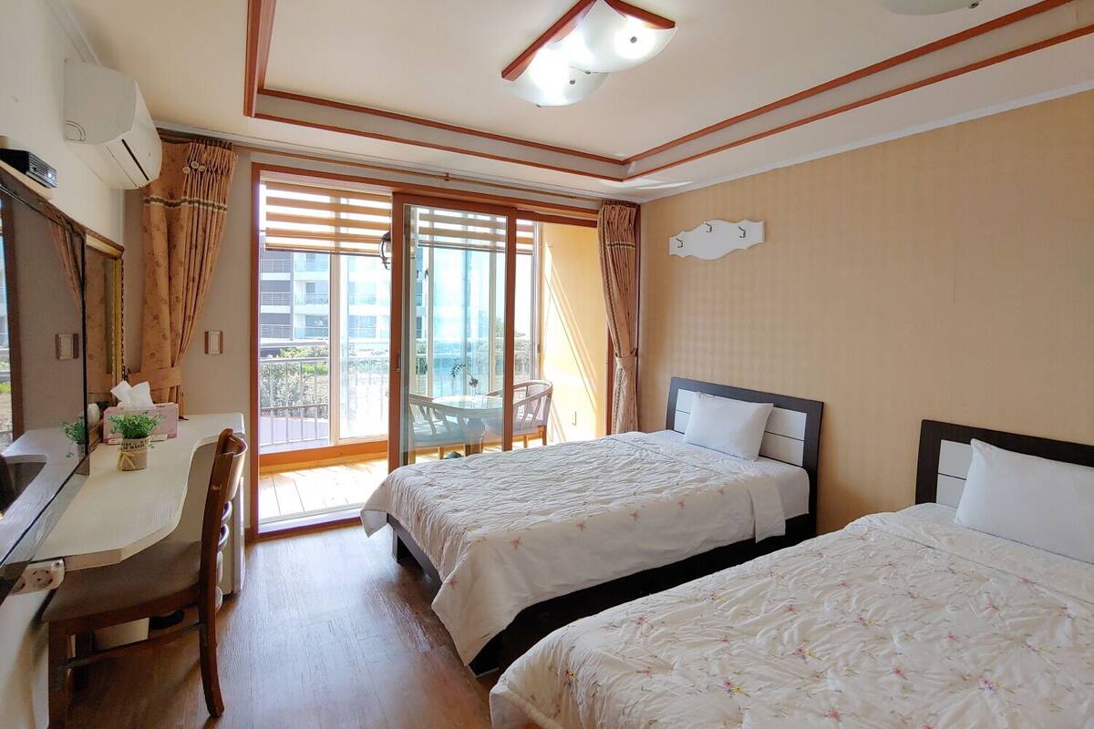A hotel room with two beds, a desk, a chair, and a balcony with curtains.