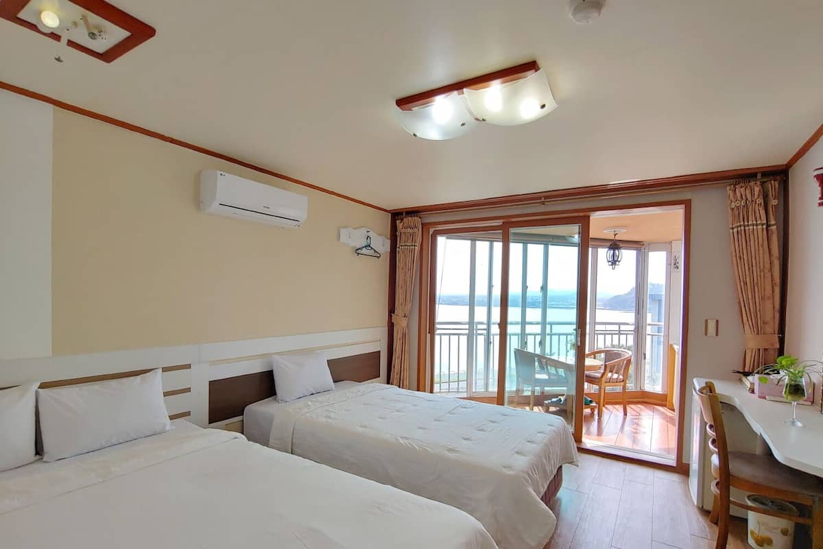 A hotel room with two beds, a balcony with a table and chairs, and a view of the sea.