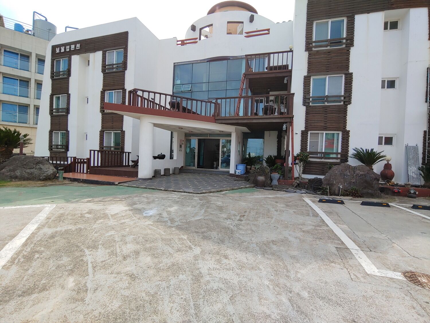 A modern multi-story residential building with a central entrance, balconies, and a covered walkway.