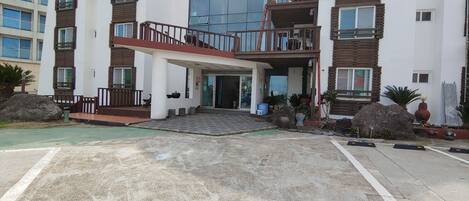 A modern multi-story residential building with a central entrance, balconies, and a covered walkway.