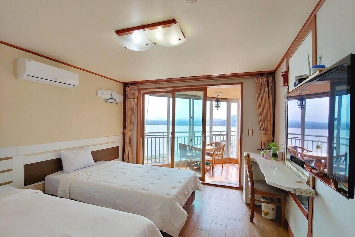 A hotel room with two beds, a desk, a mirror, and a balcony with a view.
