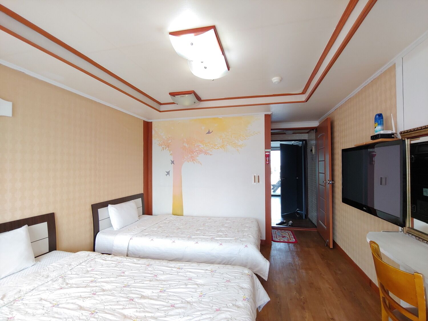 Een hotelkamer met twee bedden, een televisie, een bureau en een deur naar een gang.