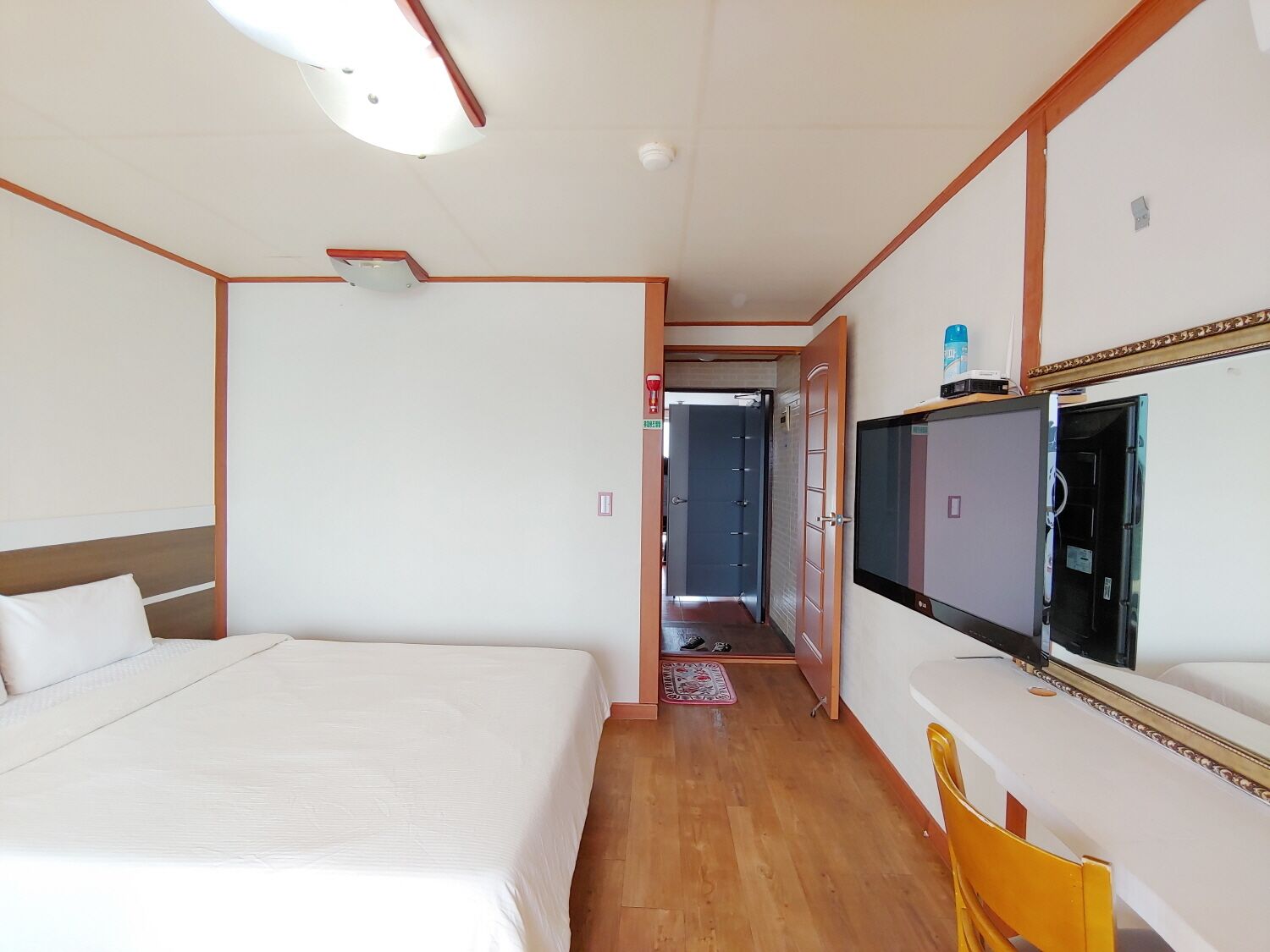 A hotel room with a bed, a desk with a chair, a television, and a bathroom visible through an open door.