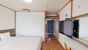 A hotel room with a bed, a desk with a chair, a television, and a bathroom visible through an open door.