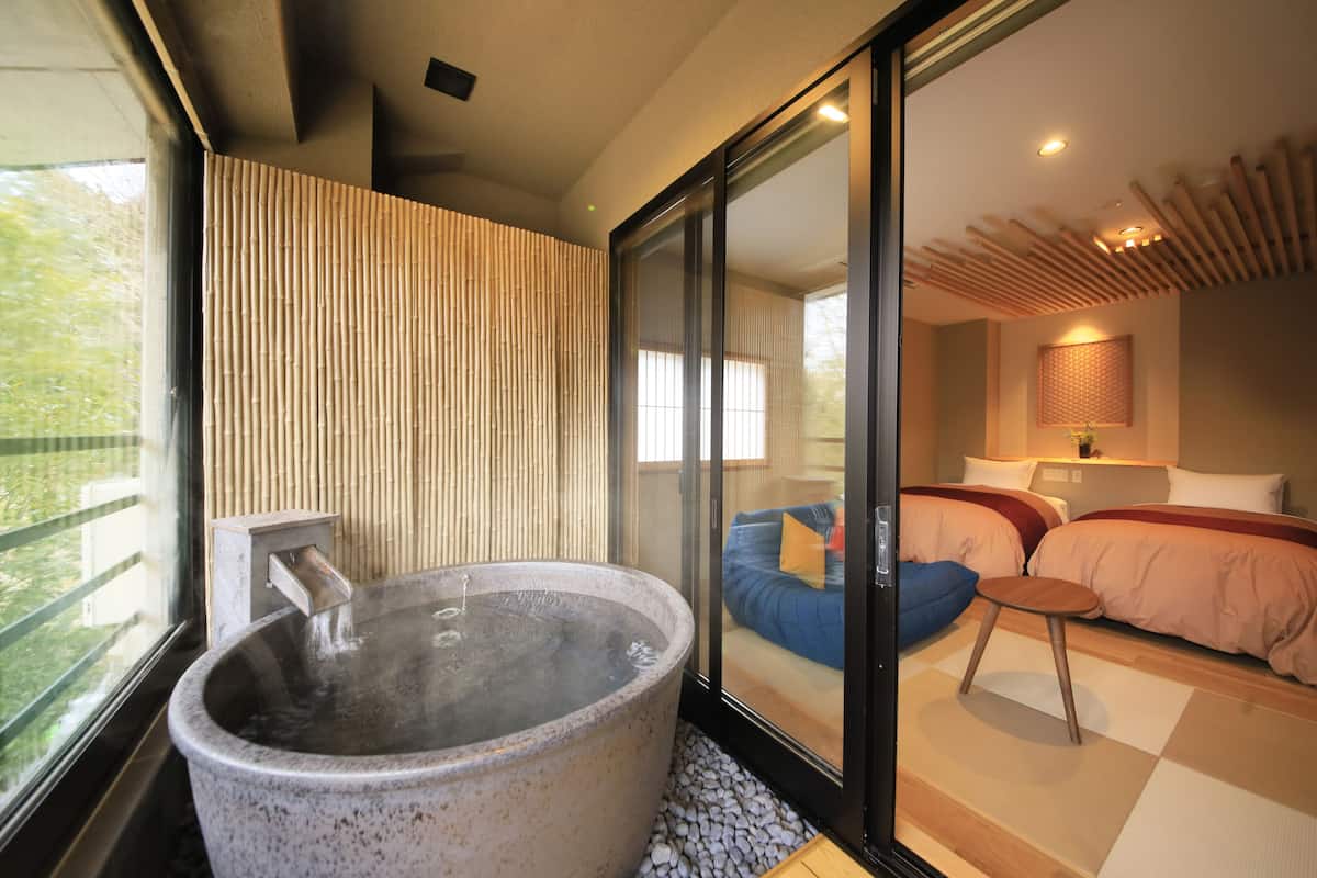 A modern room with a large hot tub, a sliding glass door leading to a bedroom with two beds and a blue sofa.