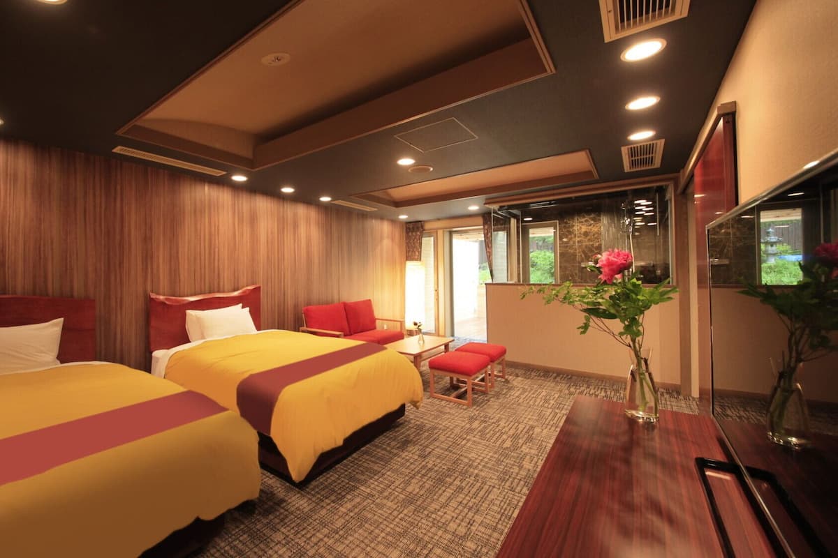 A hotel room with two beds, a small seating area, and a large window.