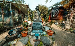 Surrounded by lush greenery, this serene setting features a central monument, a building with a glass facade, and a rustic cabin.