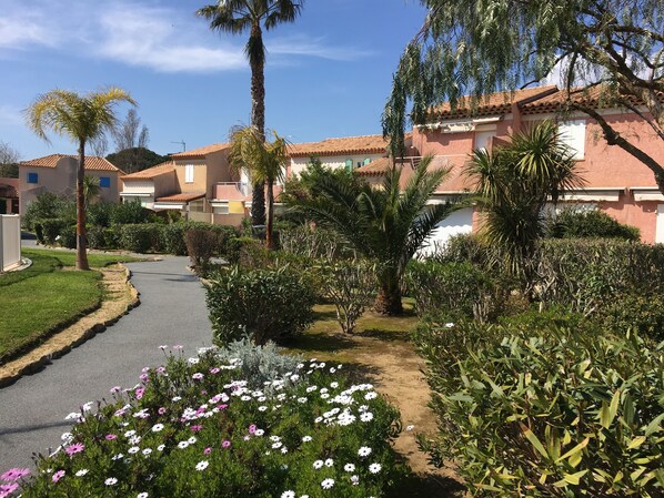 A residential area with houses, a paved road, and a variety of plants and flowers. - Air-conditioned cottage with a pool, near the beach, in a gated community (Le Lavandou)