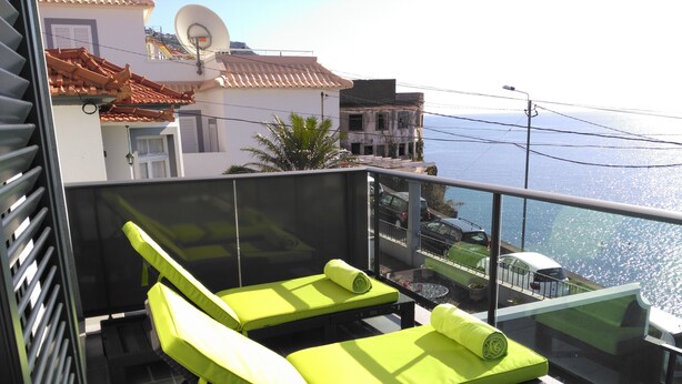 Ein Balkon mit zwei hellgrünen Liegestühlen, einem Glasgeländer und Blick auf das Meer.
