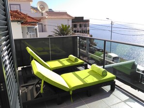 Un balcon doté de deux fauteuils de jardin d’un vert éclatant, d’une balustrade en verre et offrant une vue sur la mer.