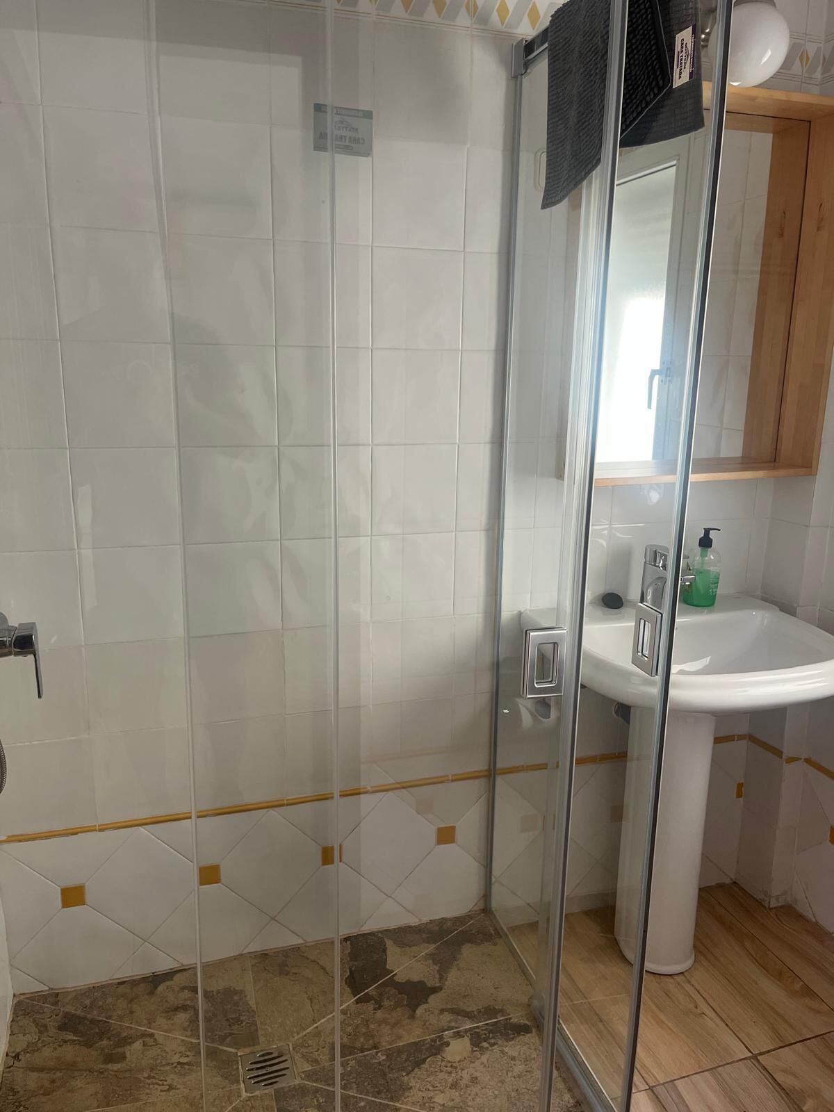 A bathroom with a glass shower enclosure, a white sink, and a wooden cabinet.