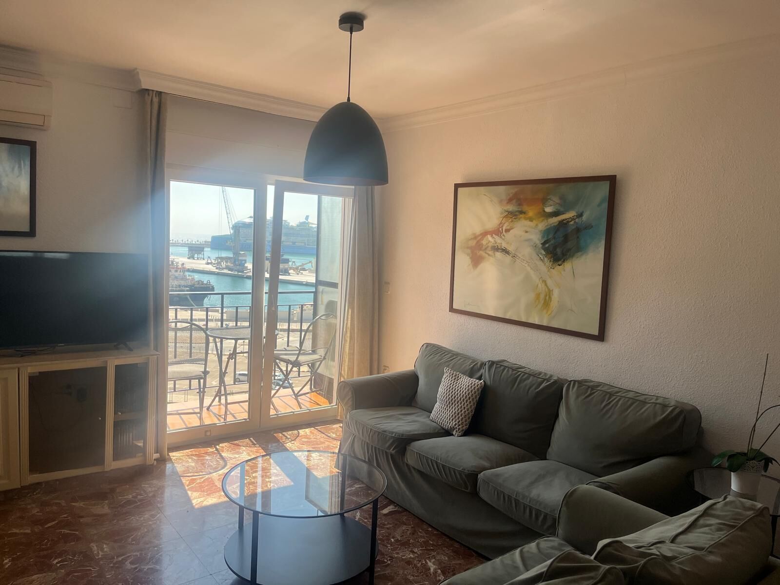 A living room with a sofa, a glass coffee table, a television, and a painting on the wall.