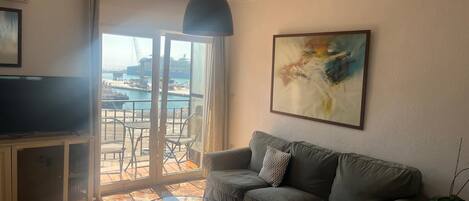 A living room with a sofa, a glass coffee table, a television, and a painting on the wall.
