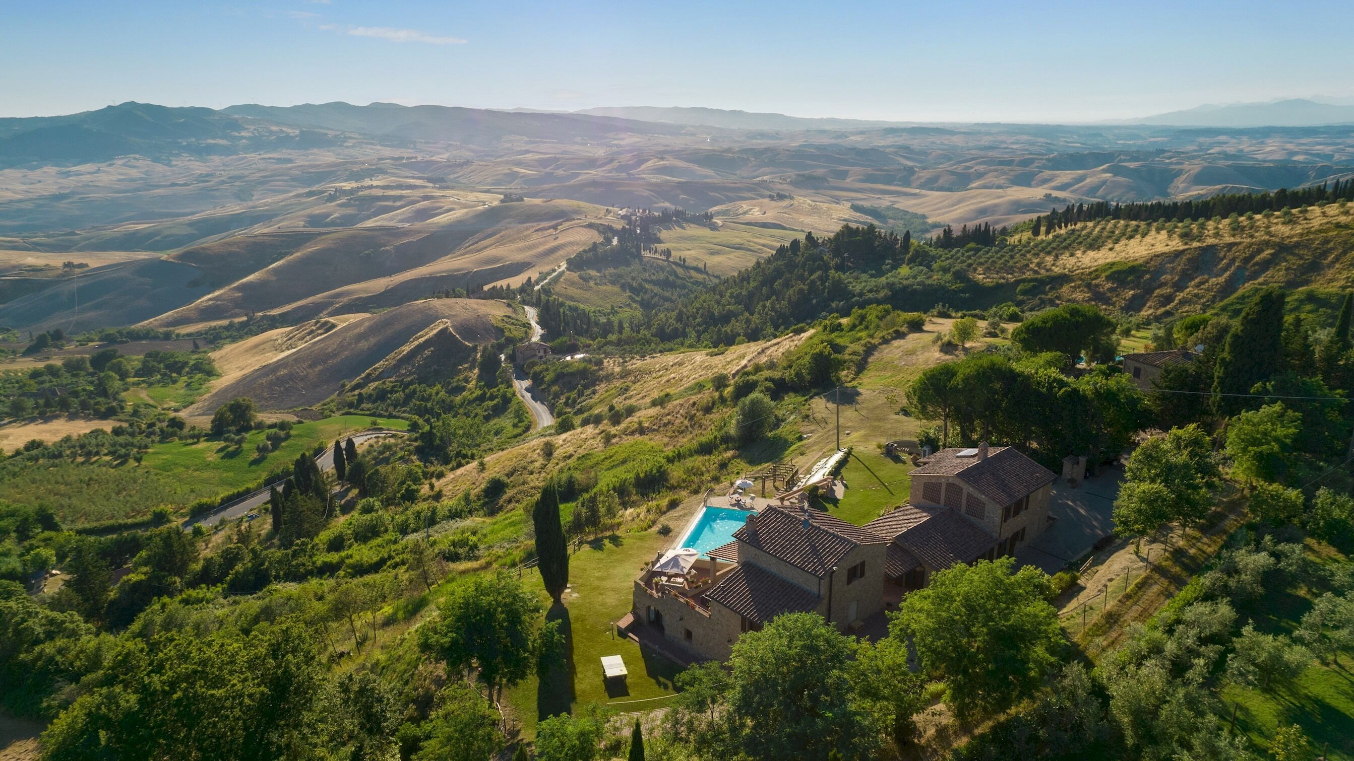 A villa with a swimming pool, surrounded by lush greenery and rolling hills.