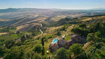 A villa with a swimming pool, surrounded by lush greenery and rolling hills.