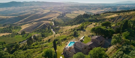A villa with a swimming pool, surrounded by lush greenery and rolling hills.