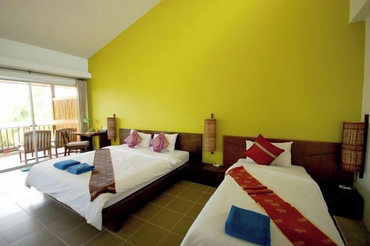 Een hotelkamer met twee bedden, een balkon en een gele muur.