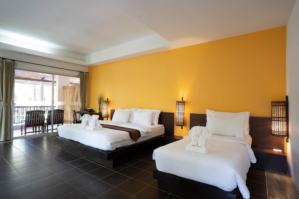 Une chambre d’hôtel avec deux lits, un balcon avec des chaises et une vue sur l’extérieur.