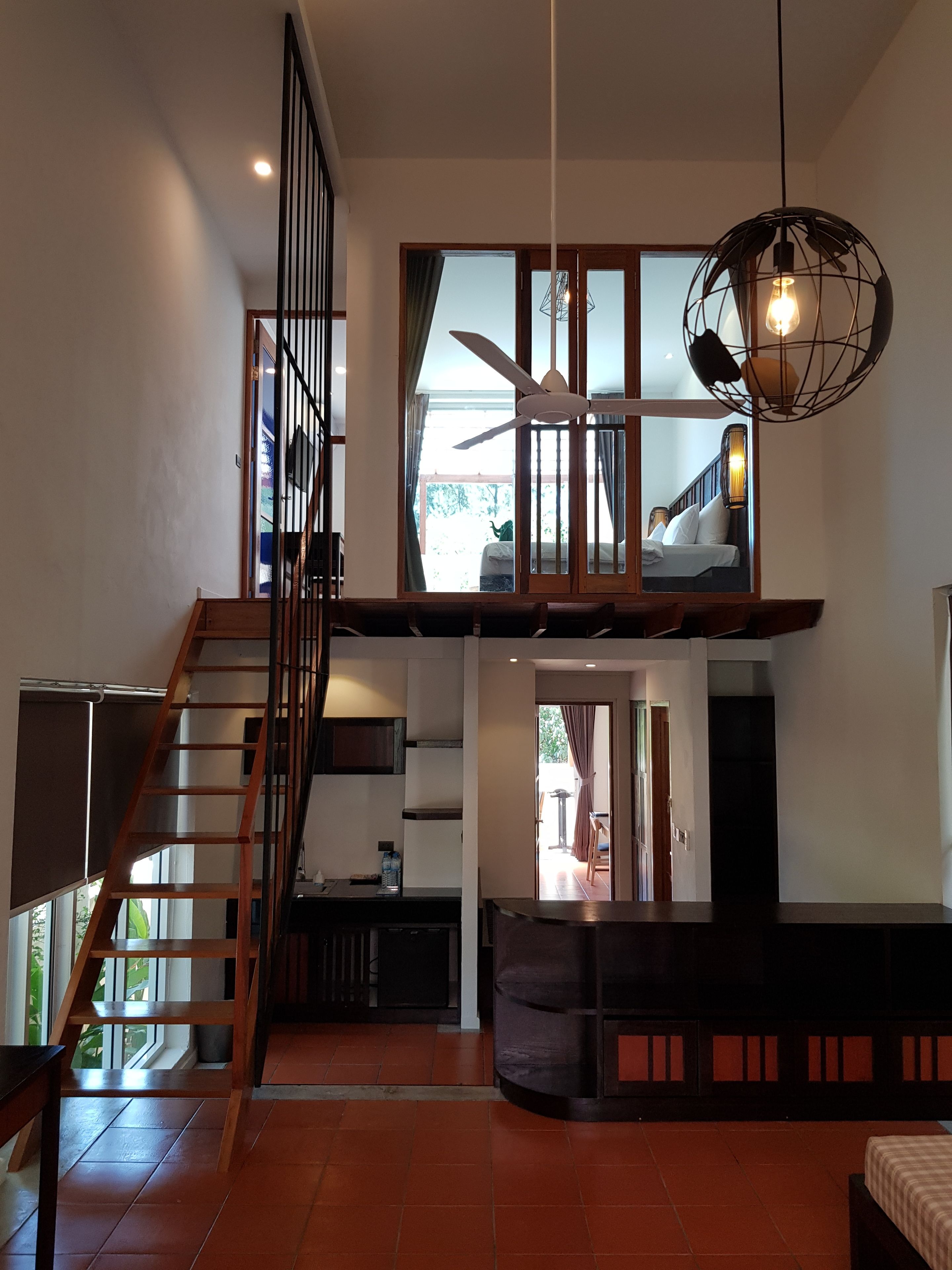 Amplia sala de estar con una escalera de madera que conduce a un nivel superior. Hay un ventilador de techo y una lámpara colgante.