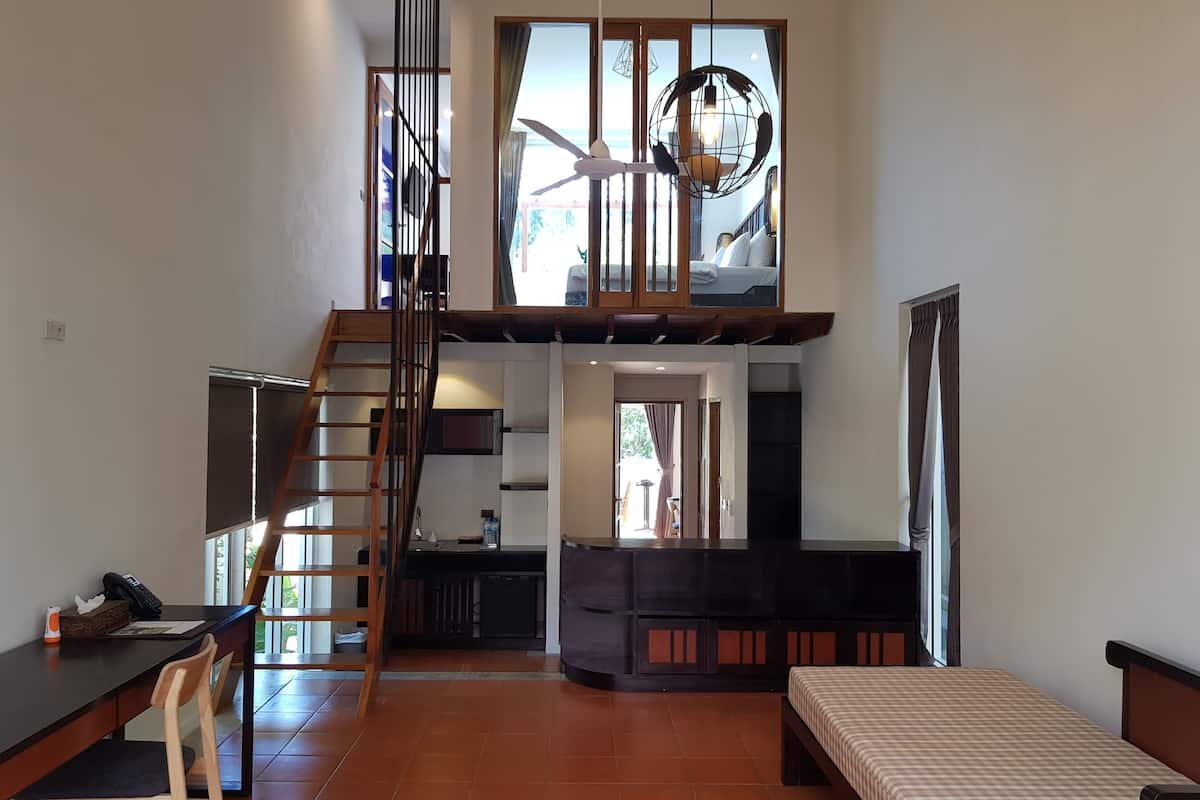 Une chambre spacieuse aménagée en loft, avec un grand lit, un bureau et un escalier menant à un niveau supérieur.