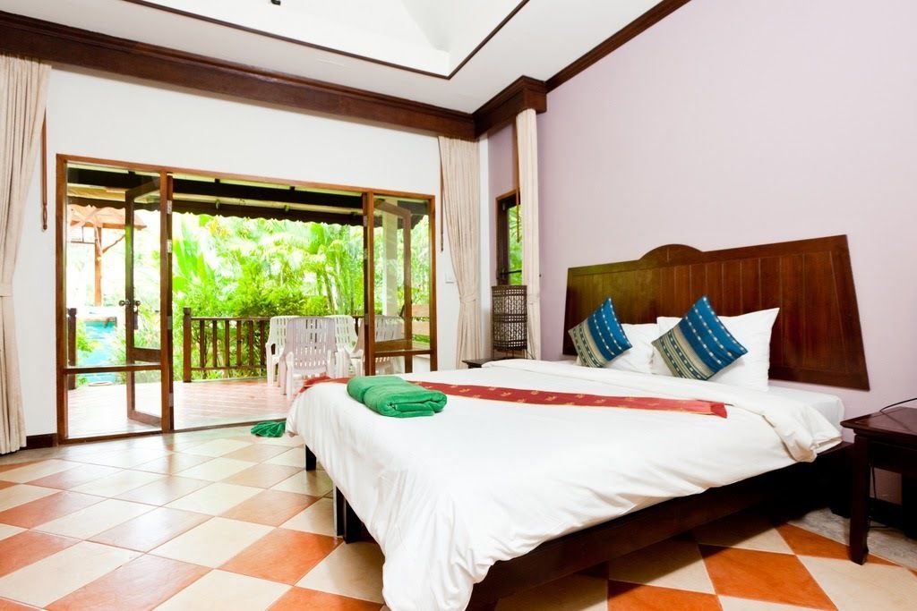 A hotel room with a large bed, a wooden headboard, and a view of lush greenery through the sliding glass doors.