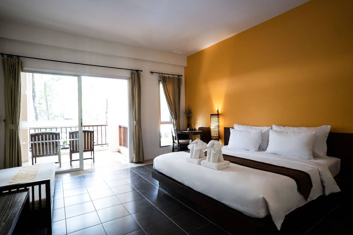 Une chambre d’hôtel avec un grand lit, un bureau, une chaise et un balcon avec des rideaux.