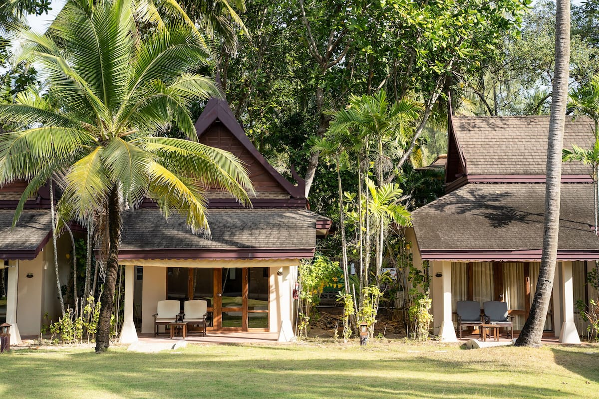 Un bungalow doté d’une véranda, de deux chaises et d’un palmier.