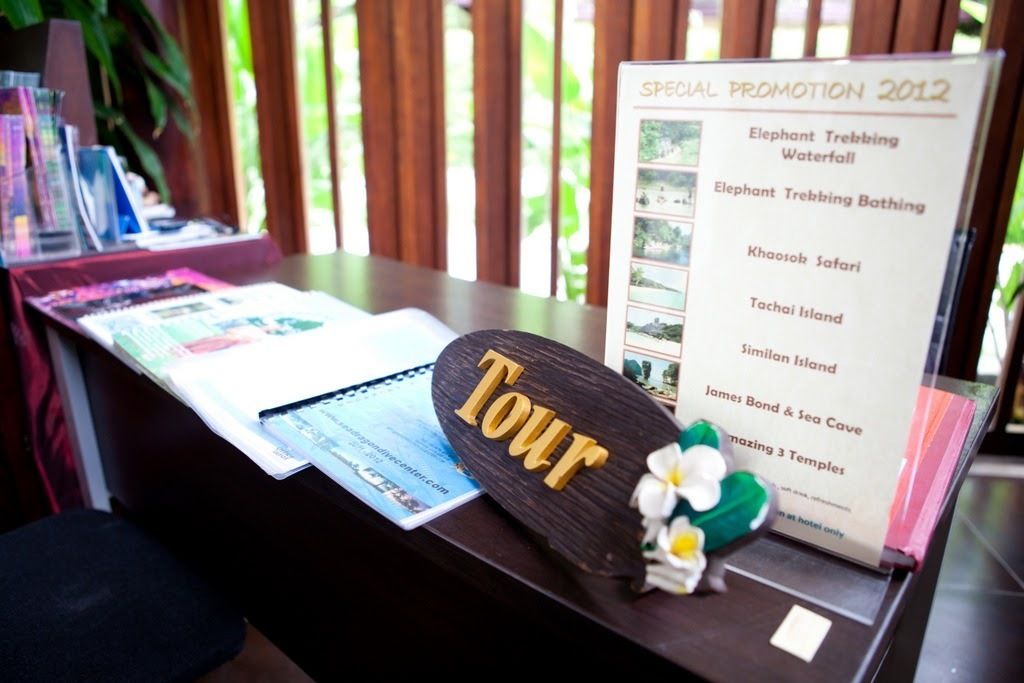 A reception desk with a sign listing special promotions for 2012, including activities like Elephant Trebbing and Bathing, and tours to James Bond & Sea Cave and 3 Temples.