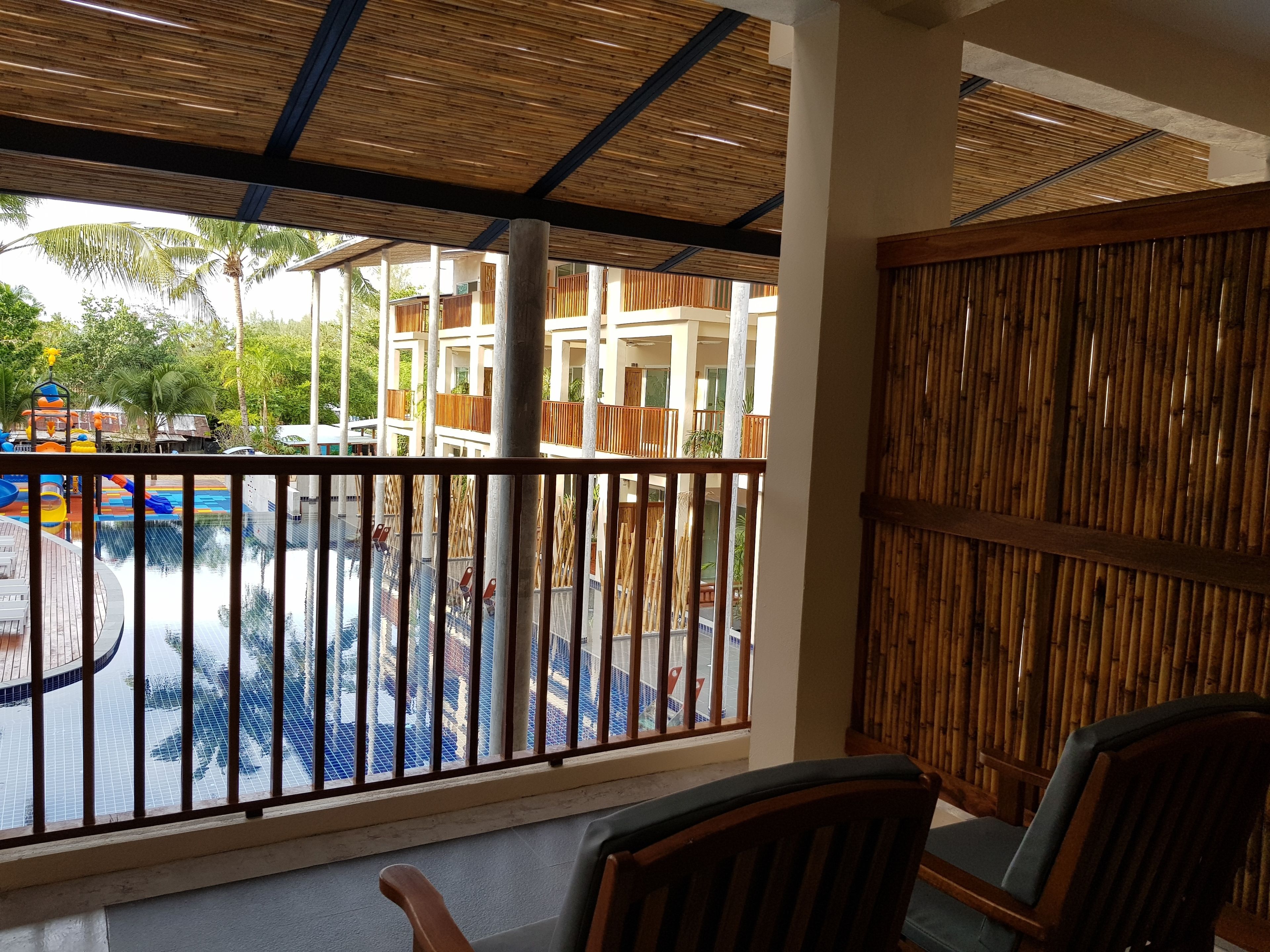 A pool area with a view of a building with multiple balconies, a wooden fence, and a chair in the foreground.