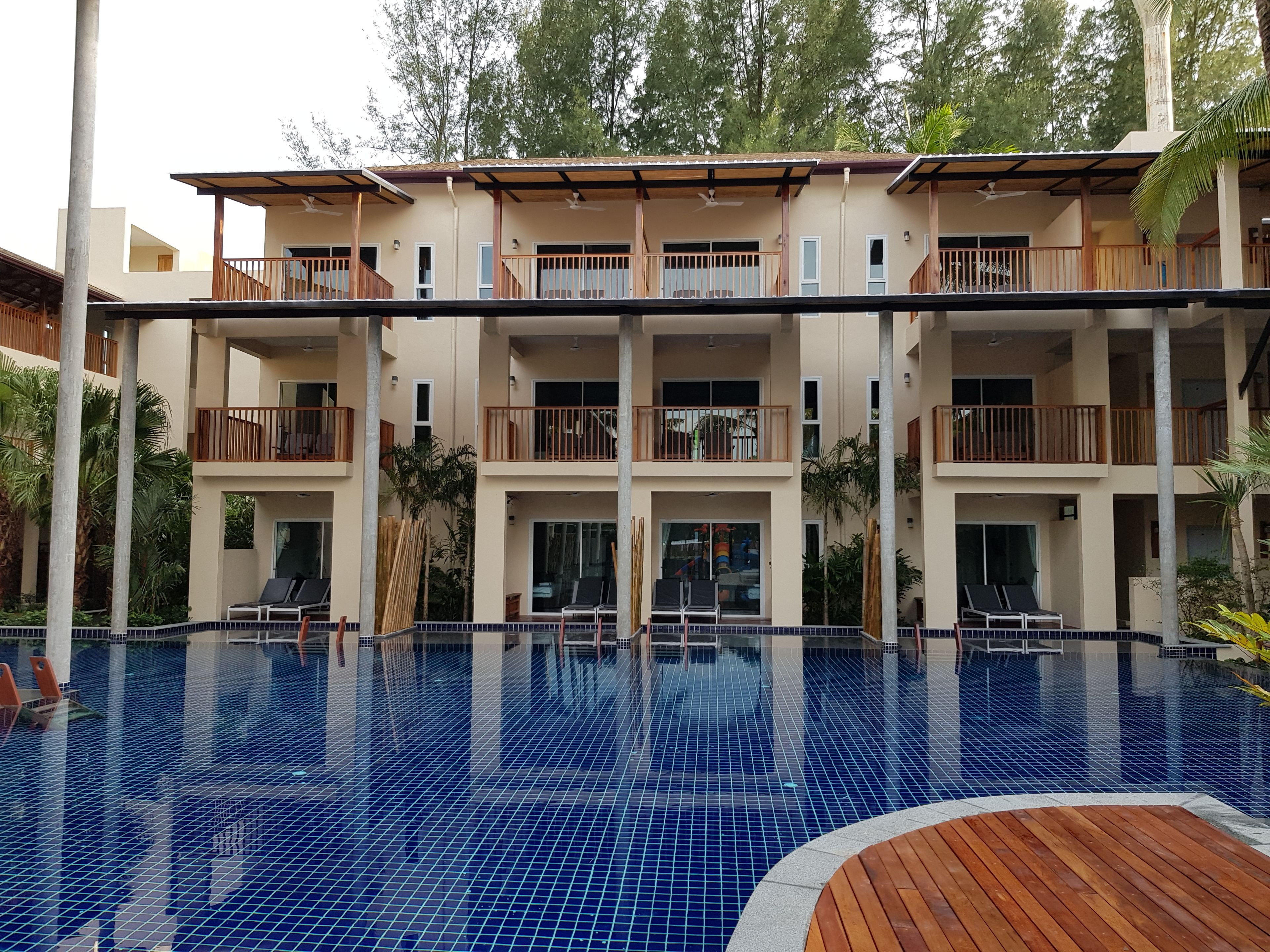 Un hotel de varios pisos con piscina, balcones y una terraza de madera.