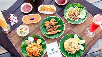 A table with various dishes and drinks, including noodles, fish, and rice, on a wooden table with a placemat.