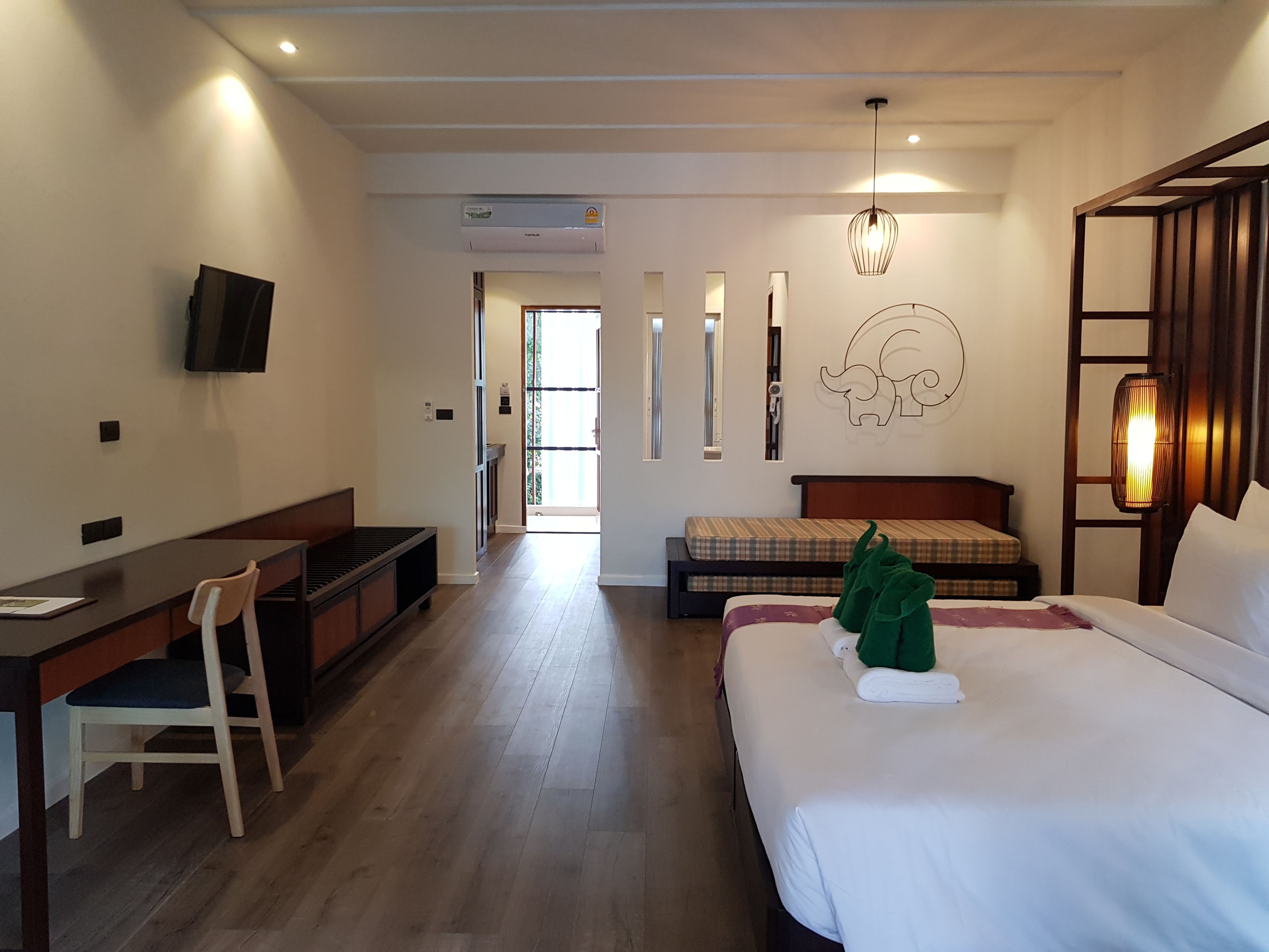 A hotel room with a bed, a desk, a chair, a television, and a wall-mounted air conditioner.