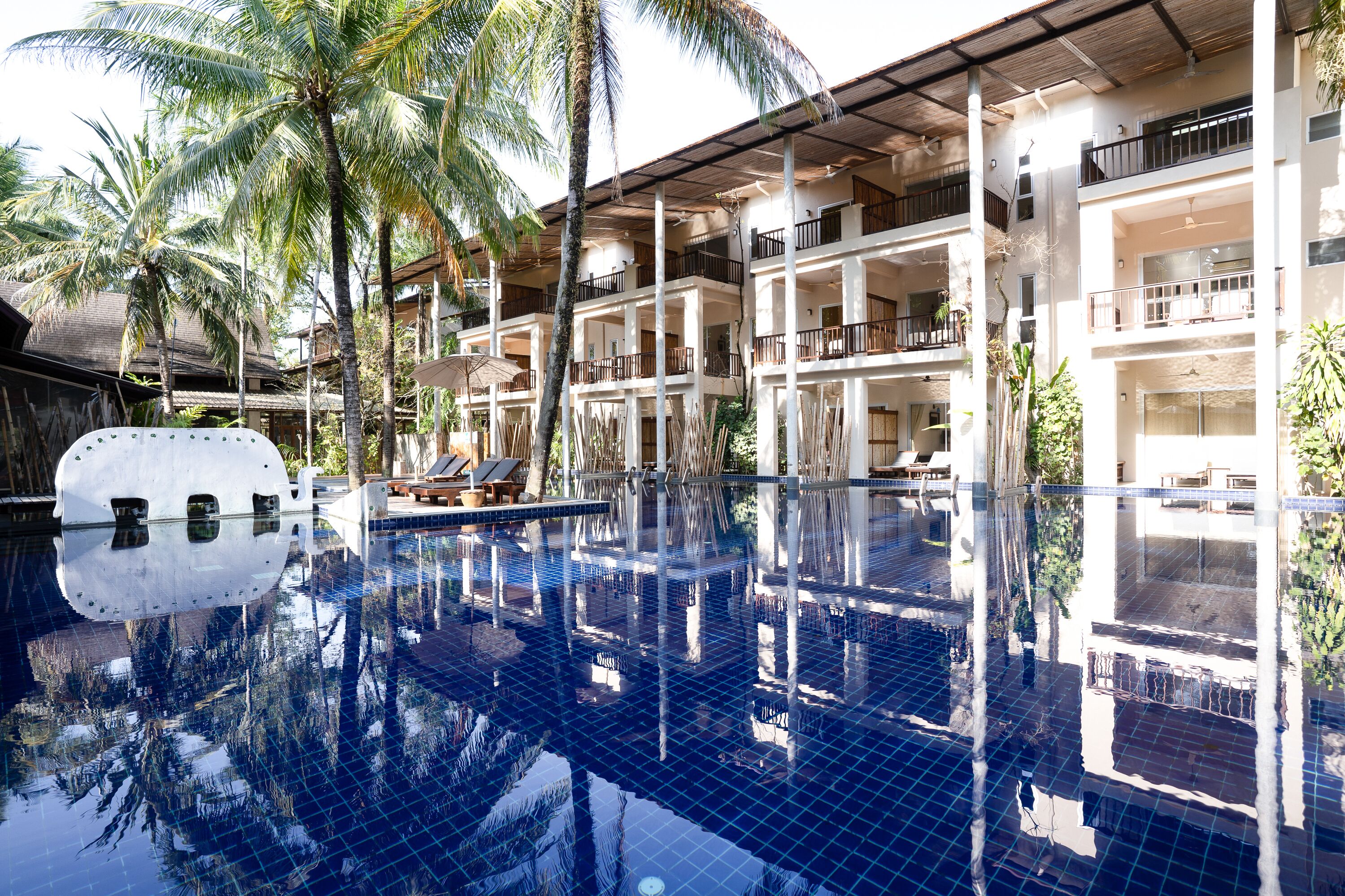 A hotel with a large indoor swimming pool surrounded by palm trees, multiple balconies, and a covered outdoor seating area.
