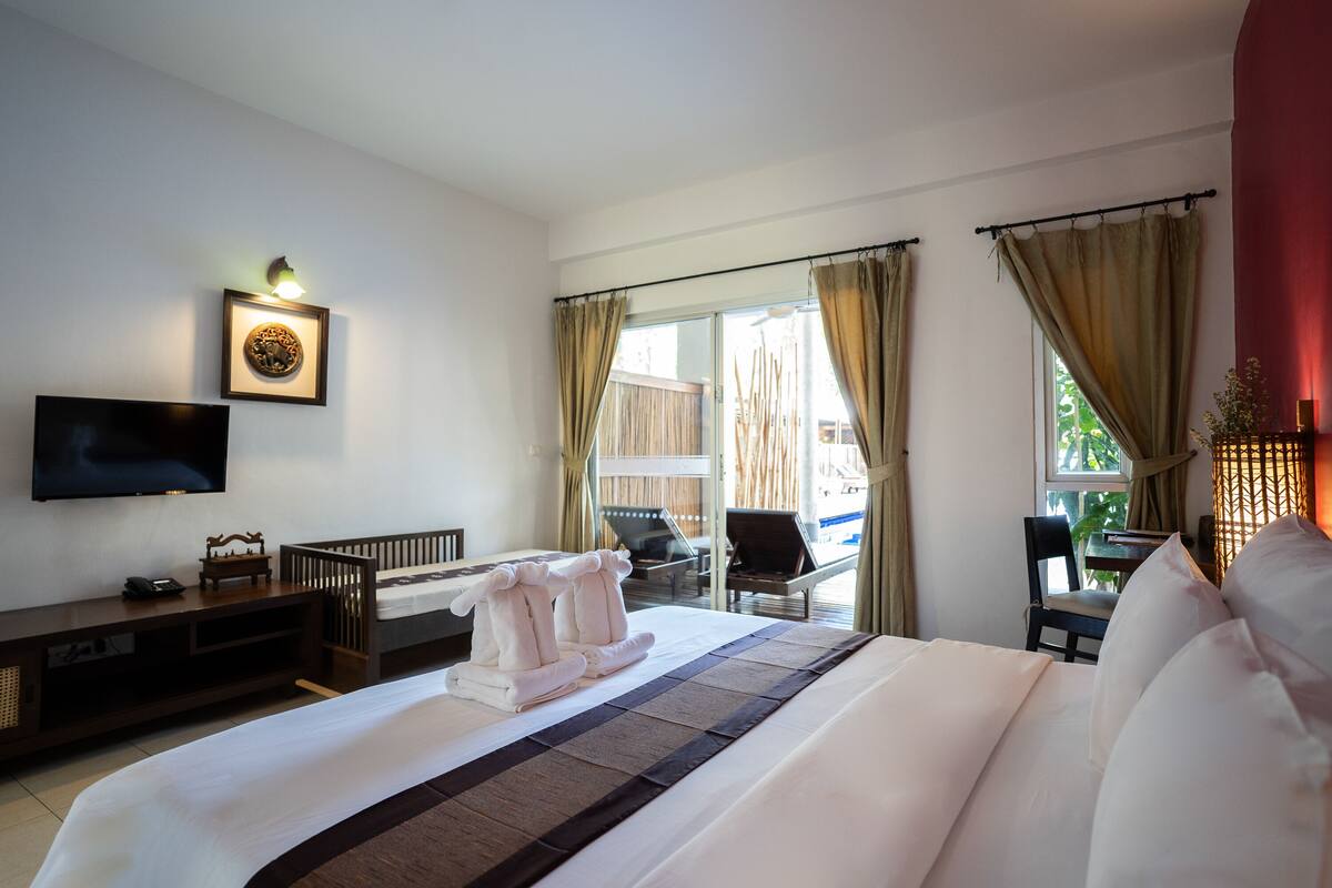 Une chambre d’hôtel avec un lit, une télévision, un bureau et un balcon avec des rideaux.