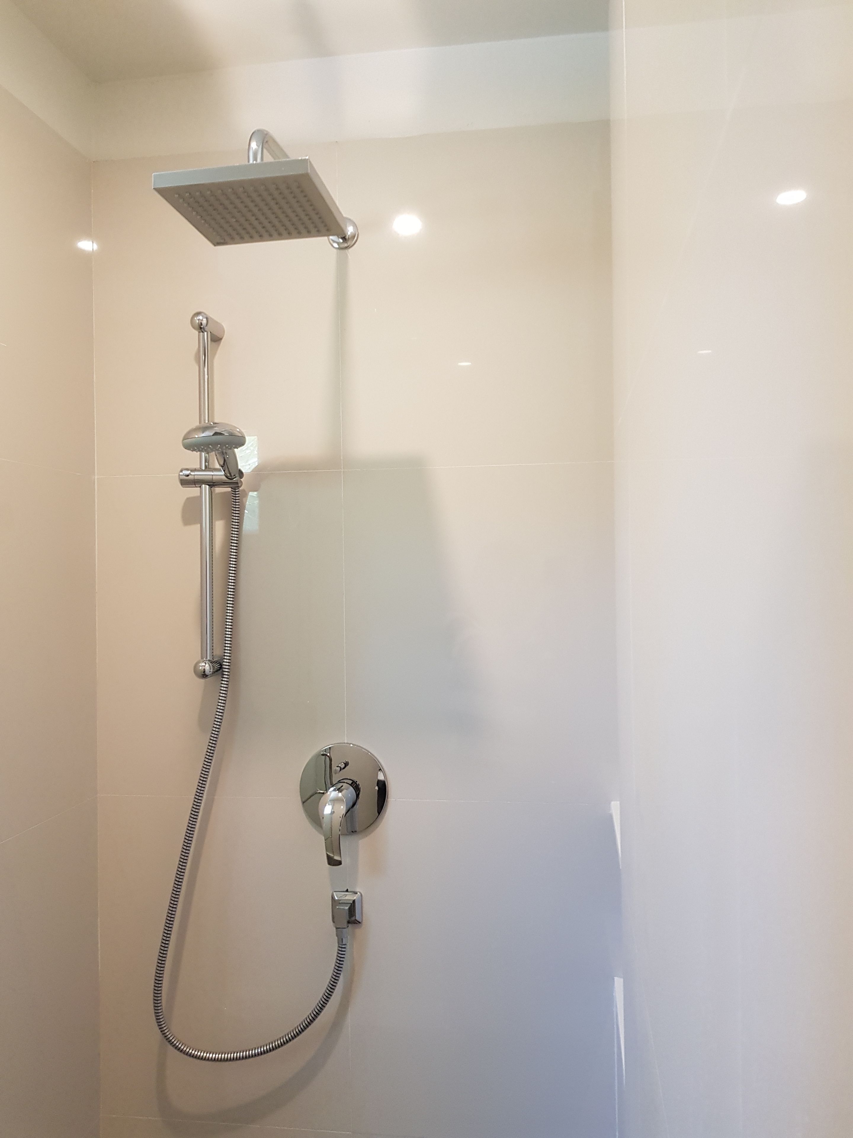 A modern shower with a handheld showerhead, a fixed showerhead, and a wall-mounted control valve.